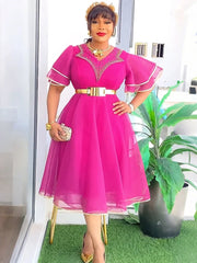 A woman wears a fuchsia knee-length dress with ruffle sleeves, a gold belt, and beaded neckline.