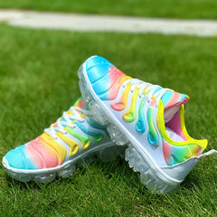 A pair of rainbow-colored mesh sneakers with transparent rubber soles sitting on green grass.