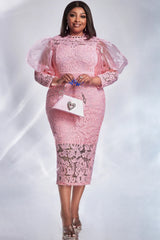 A woman wears a pink lace midi dress with sheer puff sleeves and a heart-shaped handbag.