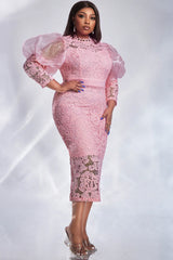 A woman wears a pink lace midi dress with sheer puff sleeves and a slim fit.