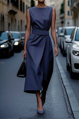 A woman wears a sleeveless, navy blue ankle-length dress with an asymmetrical waist-closing design.