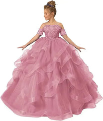 A girl wears a dusty pink off-shoulder ball gown with floral appliques and a ruffled tulle skirt.