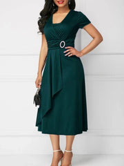 A woman wears a dark green short-sleeved midi dress with a V-neck and an asymmetric hem.
