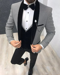 A man wears a black and white houndstooth suit jacket with a black velvet lapel, vest, and bowtie.