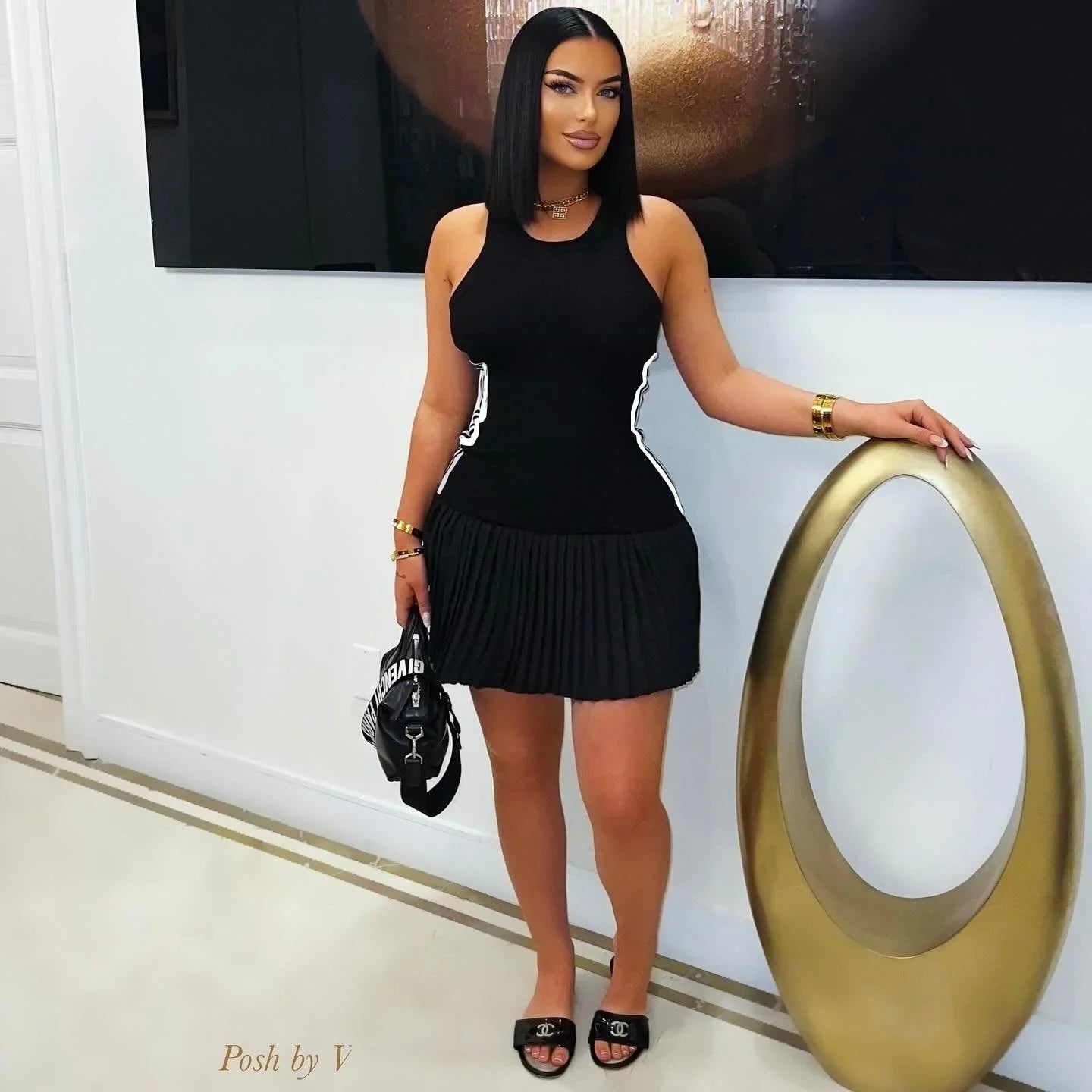 A woman wears a black sleeveless mini dress with a pleated skirt and white side stripes.