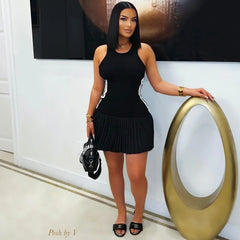A woman wears a black sleeveless mini dress with a pleated skirt and white side stripes.
