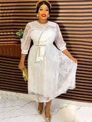 A woman wears an elegant white midi dress featuring sheer polka-dot sleeves and a belted waist.