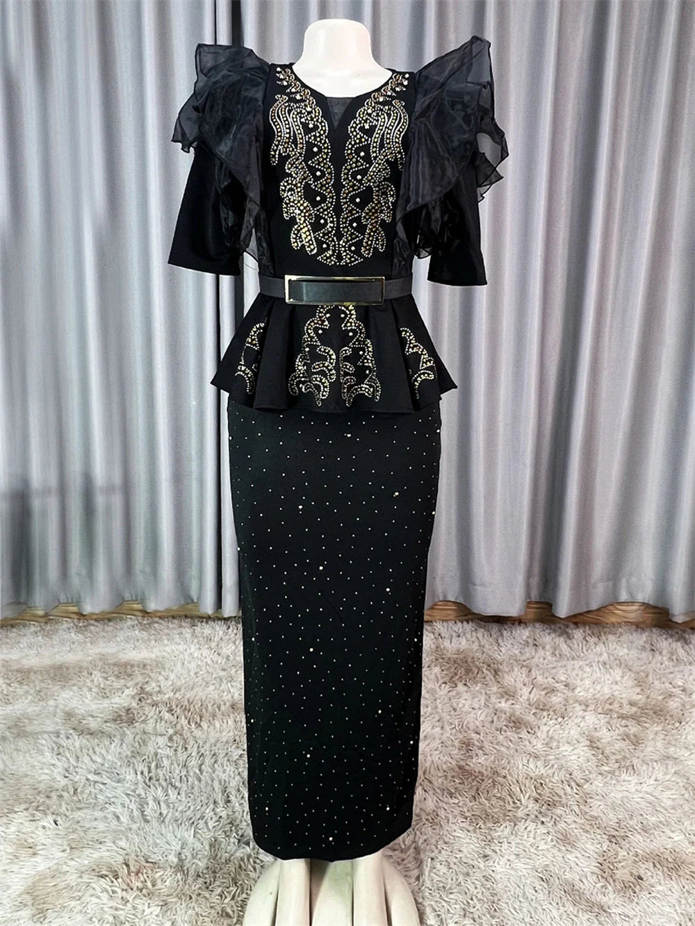 A black ankle-length dress with gold rhinestone embellishments, ruffled sleeves, and a belt.