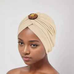 A beige pleated turban headscarf featuring a decorative amber-colored crystal brooch.