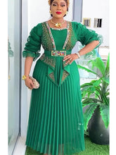 A woman wears an elegant emerald green pleated maxi dress with embellished bodice and puff sleeves.