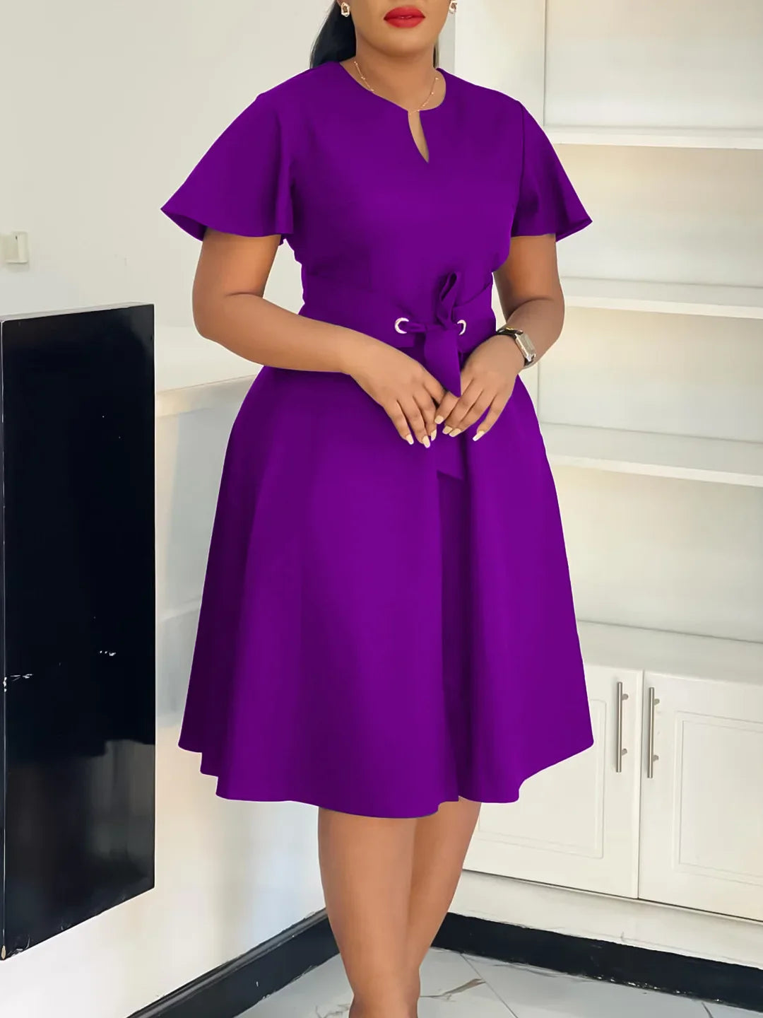 A woman wears a knee-length purple A-line dress with short sleeves and a lace-up waist detail.