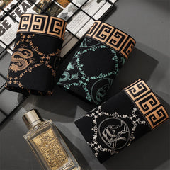 Three pairs of black boxer shorts with gold Greek key waistbands and ornate printed designs.