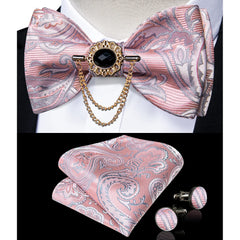 A pink paisley bow tie set featuring a decorative brooch, pocket square, and matching cufflinks.