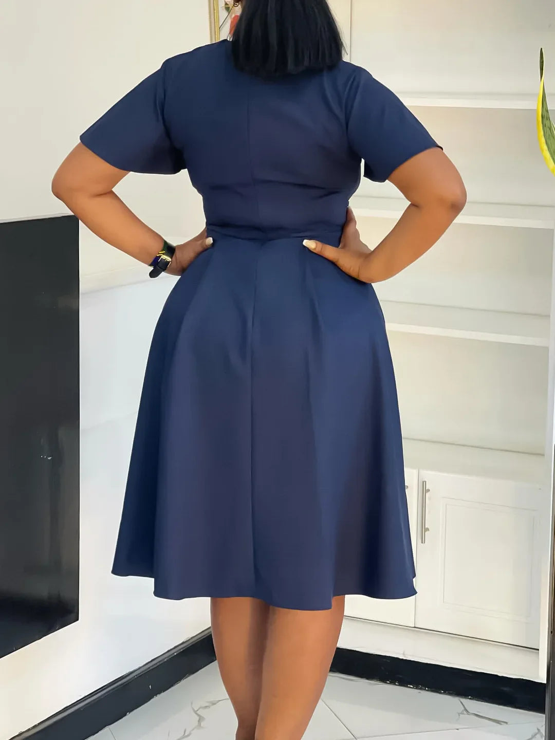 A woman wears a navy blue short-sleeved knee-length A-line swing dress from the back.