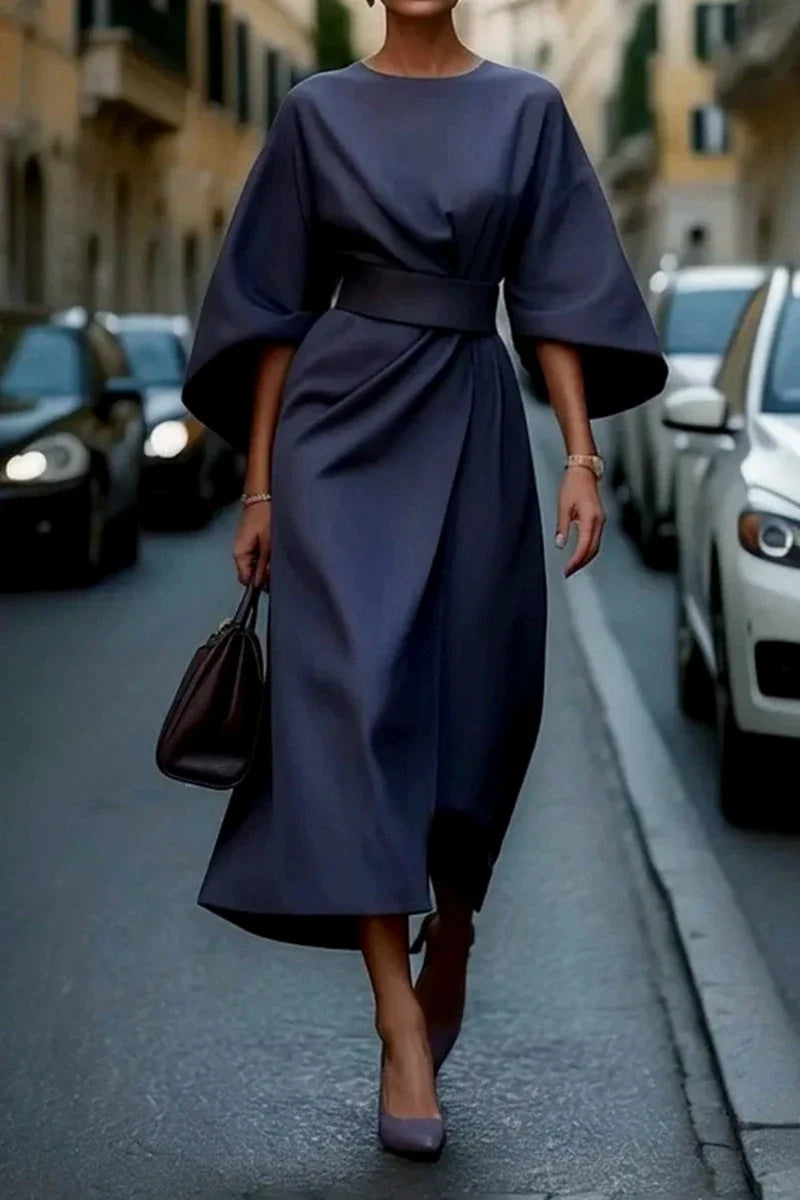 A woman wears an elegant navy blue ankle-length dress with bat sleeves and a cinched waist.