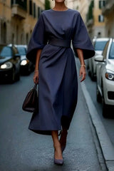A woman wears an elegant navy blue ankle-length dress with bat sleeves and a cinched waist.