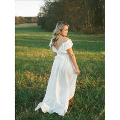 A woman wears a white off-shoulder bohemian maxi dress with ruffled sleeves in a grassy field.