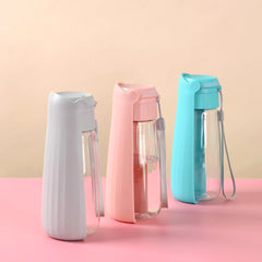 Three portable pet water bottles in gray, pink, and turquoise stand on a pink surface.