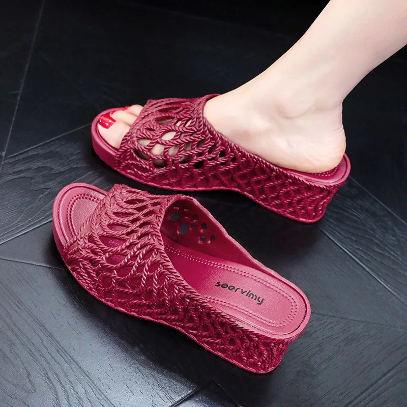 A pair of burgundy wedge slippers with a hollow-out woven design and a peep-toe front.