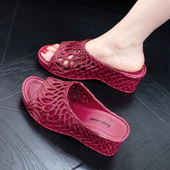 A pair of burgundy wedge slippers with a hollow-out woven design and a peep-toe front.