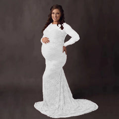 A pregnant woman wears a white, long-sleeved lace mermaid maternity gown with a long train.
