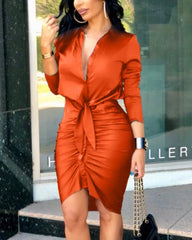 A woman wears a long-sleeved, orange bodycon mini dress with a deep V-neck and front tie detail.