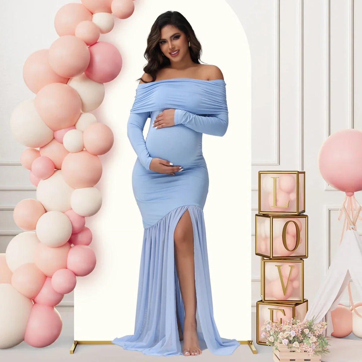 A pregnant woman wears a light blue off-shoulder maternity gown with long sleeves and a side slit.