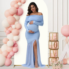 A pregnant woman wears a light blue off-shoulder maternity gown with long sleeves and a side slit.