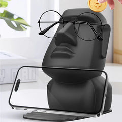 A black Moai statue desk organizer holding a pair of glasses and a smartphone.