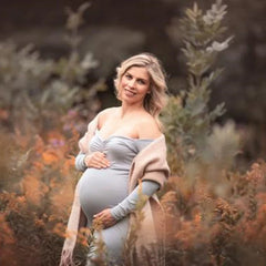 A pregnant woman wears a long-sleeved, ankle-length grey maternity dress in a field.
