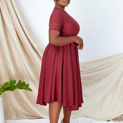 A plus size burgundy short-sleeved A-line dress with a pleated skirt.