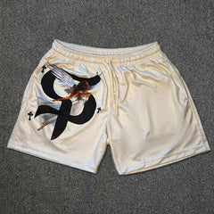 Cream-colored basketball shorts featuring a black graphic of a winged goddess and small crosses.