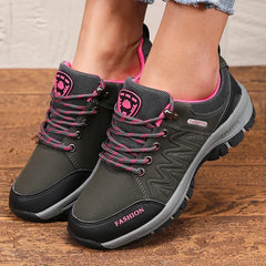 A pair of grey and black women's hiking sneakers with pink accents and lace-up closures.
