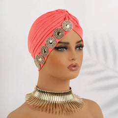 A coral pleated turban headscarf decorated with a row of circular rhinestone embellishments.