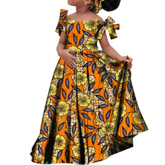 A girl wears a long, orange African-print dress with yellow flowers and a matching headscarf.