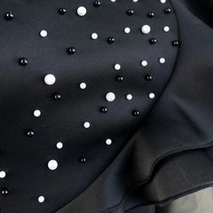 A black sheath dress featuring a scattered pattern of white and black pearl embellishments.