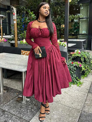 A woman wears a long-sleeved, burgundy A-line dress with a lace bodice and square neckline.
