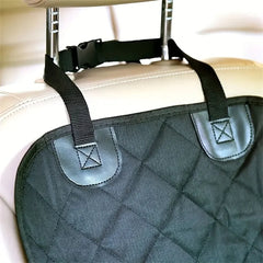 A black quilted fabric dog car seat cover attached to the headrest of a light-colored car seat.