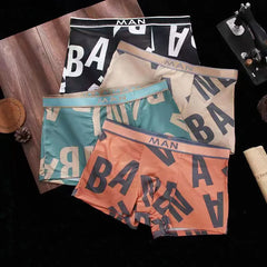 Four pairs of men's boxer shorts in black, beige, green, and orange with a repeating letter print.