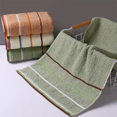 A stack of three folded striped cotton towels sits next to a matching green towel draped over a basket.