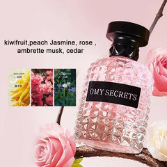 A bottle of Omy Secrets perfume with a textured glass design sits among pink roses.