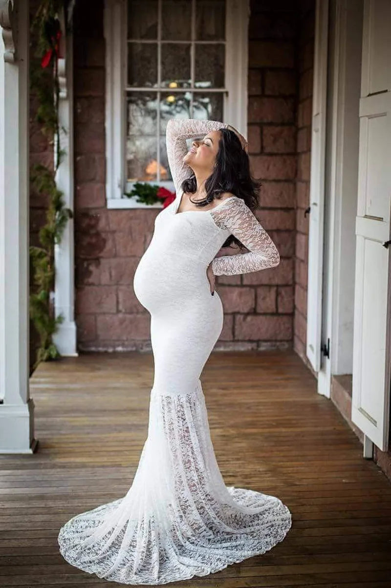 A pregnant woman wears a white, long-sleeved, lace mermaid-style maternity gown.