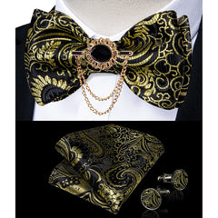 A black and gold paisley bow tie set with a decorative brooch, pocket square, and cufflinks.