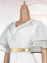 A white mesh maxi dress featuring gold-trimmed ruffle sleeves, a metallic belt, and beaded neckline.