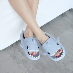 A pair of light blue shark-shaped EVA slides worn on a person's feet.