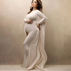 A pregnant woman wears a long-sleeved, ankle-length cream maternity dress with a flowing skirt.