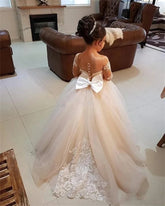 A young girl wears an elegant floor-length tulle flower girl dress with a large back bow and lace.