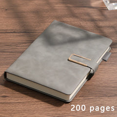 A grey A5 leather notebook with a gold metal clasp closure resting on a wooden surface.