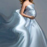 A pregnant woman wears a flowing, light blue satin gown with a long, billowing train.