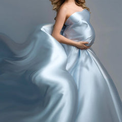 A pregnant woman wears a flowing, light blue satin gown with a long, billowing train.